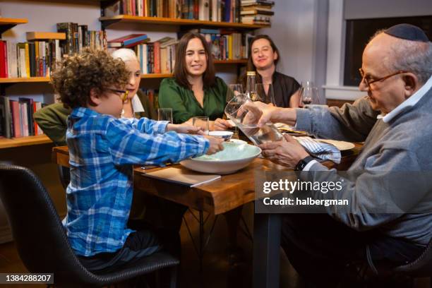 großvater hilft kleinem jungen, sich beim pessach-seder mit der familie die hände zu waschen - judaism stock-fotos und bilder