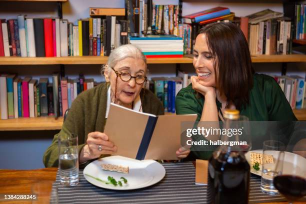 two women reading from haggadah at passover seder - passover stockfoto's en -beelden