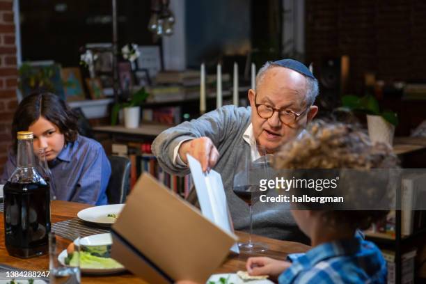 grandfather helping little boy read from haggadah at pasover seder - judeu imagens e fotografias de stock