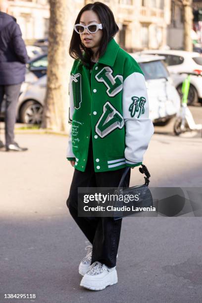 Guest wearing a green and white bomber jacket, black jeans, blue bag and white shoes, is seen outside Chanel, during Paris Fashion Week - Womenswear...