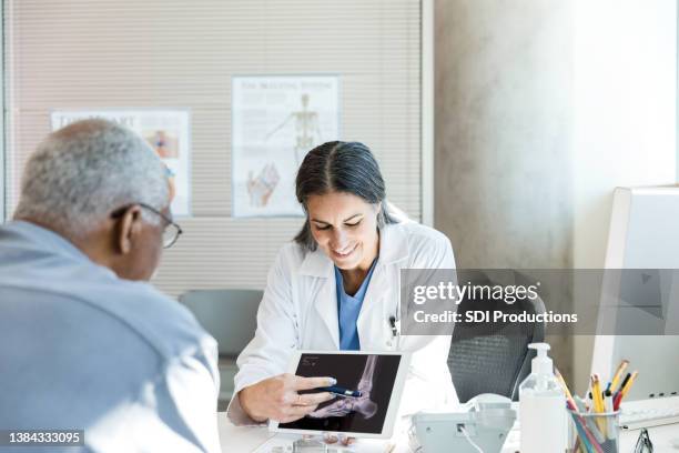 orthopedic surgeon uses x-ray displayed on tablet to help patient - ortopedista imagens e fotografias de stock