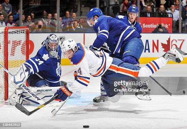 James Reimer of the Toronto Maple Leafs defends the goal as teammate Dion Phaneuf checks Taylor Hall of the Edmonton Oilers during NHL game action...