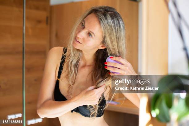 woman brushing hair in front of bathroom mirror - brushing hair stock-fotos und bilder