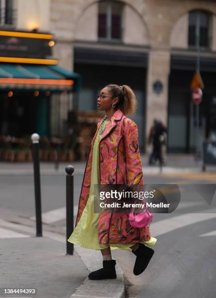 Petra Henriette Rufi wearing silver shades, silver earrings and chains, a pink long coat with pattern, a yellow maxi dress, a pink leather bag and...