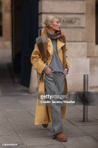 Amalie Gassmann wearing a yellow long coat, a colorful scarf, a grey sweater, grey pants and UGG chestnut Classic Mini II Boot on March 04, 2022 in...