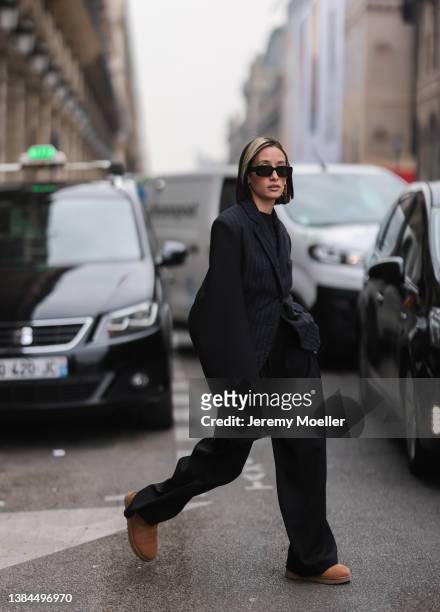 Alexandra Guerain wearing black shades, gold earrings, a black blazer, a black shirt, black wide pants and UGG chestnut Classic Mini II Boot on March...