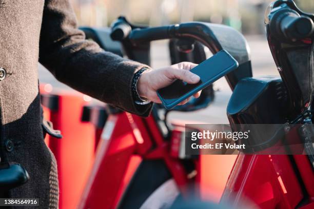 elegant businessman using smartphone to rent a city bike on his way to work - bicycle rental stockfoto's en -beelden
