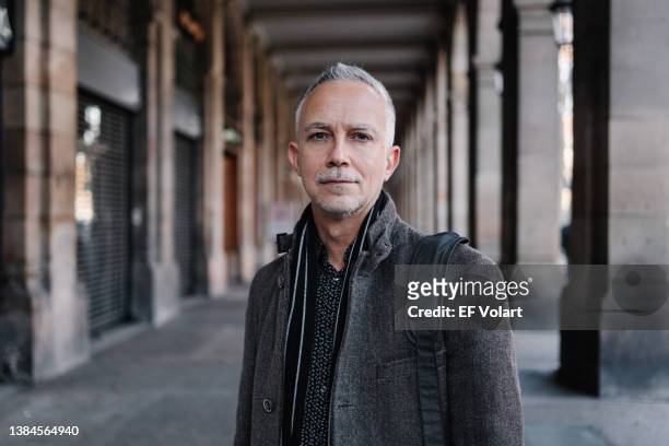 portrait of serious mature professional businessman with grey white hair and beard looking to camera in old european city - visage homme photos et images de collection