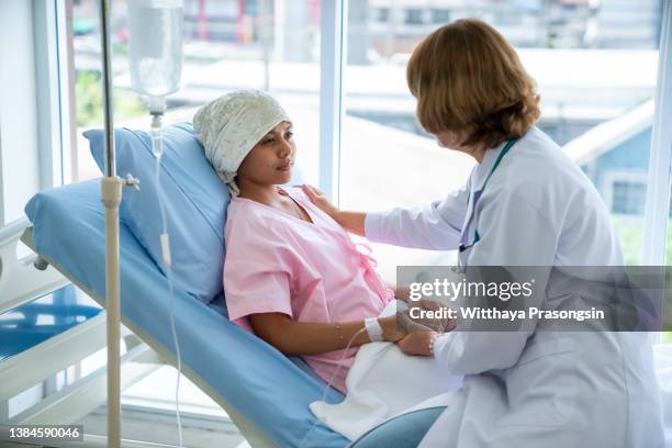 a female doctor encourages a young woman with cancer by holding hands on the patient's bed. - radiotherapy stock pictures, royalty-free photos & images