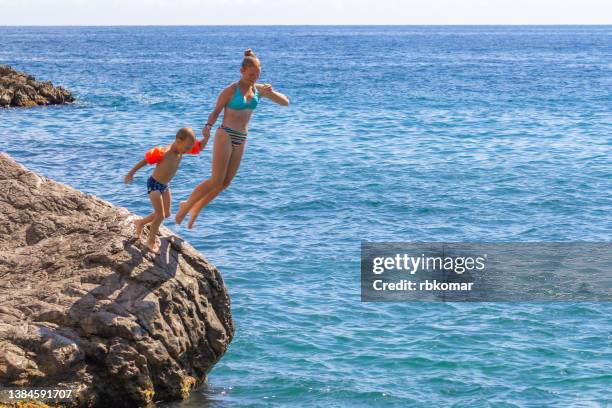 fun activities for children during their summer vacation at the sea. joint diving into the water from a high stone - salto desde acantilado fotografías e imágenes de stock