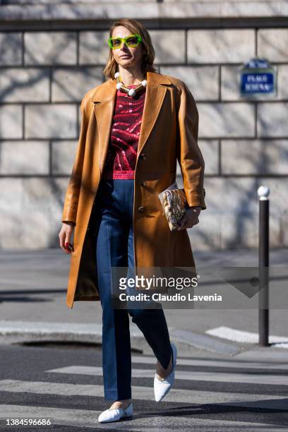 Guest wearing a red printed jumper, blue trousers, white flat shoes, camel leather jacket and green sunglasses, is seen outside Miu Miu, during Paris...