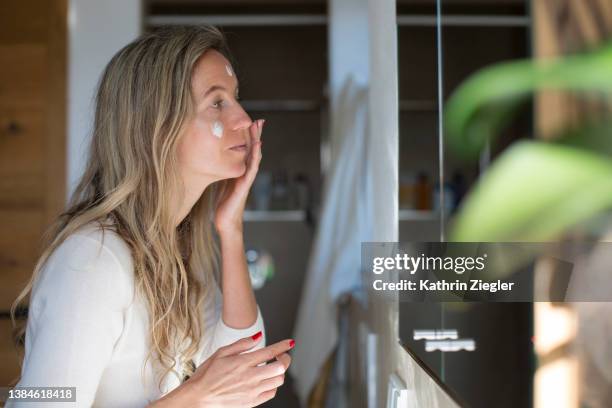 woman applying face cream in front of bathroom mirror - cream coloured 個照片及圖片檔