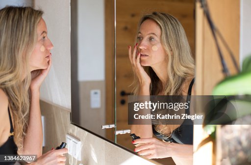 Woman applying makeup in front of bathroom mirror Woman applying makeup in front of bathroom mirror