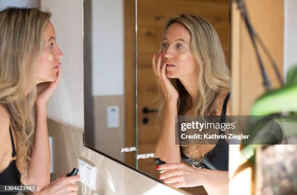 woman applying makeup in front of bathroom mirror - applying imagens e fotografias de stock