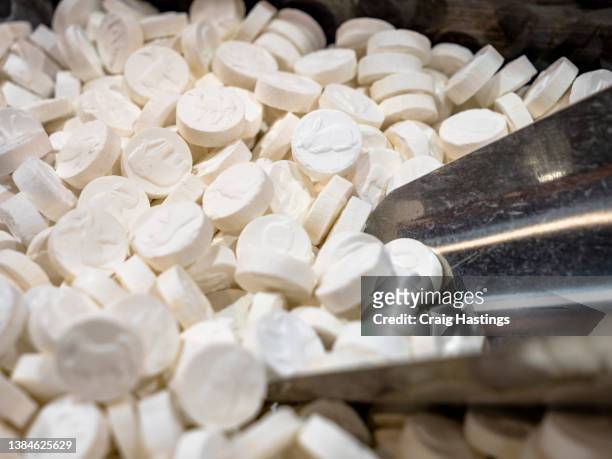 large selection of white pills resembling perscription medication, mints and illegal drugs such as mdma, yabba and acid  pictured with a serving measuring scoop. concept piece for social issues, illicit drugs, organised crime and addiction - art dealer stock-fotos und bilder