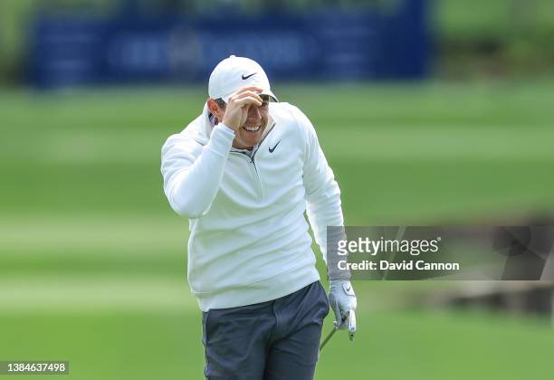 Rory McIlroy of Northern Ireland holds on to his hat in the high winds watching his second shot on the par 4, 18th hole during the weather delayed...