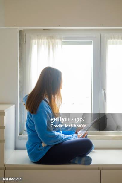 mujer leyendo un libro junto a la ventana - descontrair fotografías e imágenes de stock