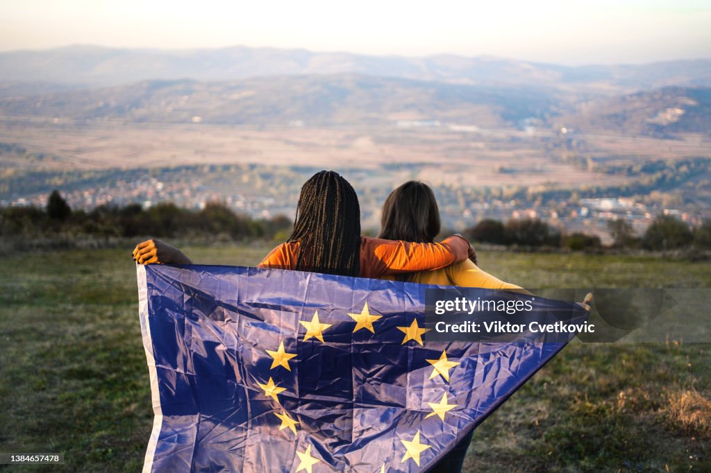Dos mujeres de pie en una colina sosteniendo la bandera de la UE a la espalda