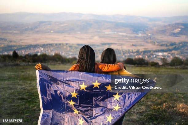 two women standing on hill holding eu flag behind back - simple living stock pictures, royalty-free photos & images