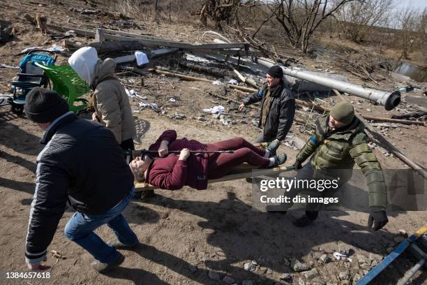 People help an elderly person cross a destroyed bridge as civilian evacuations continue in the city on March 12, 2022 in Irpin, Ukraine. Russia...