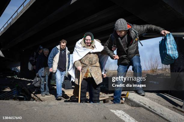 People cross a destroyed bridge as civilian evacuations continue in the city on March 12, 2022 in Irpin, Ukraine. Russia continues its assault on...