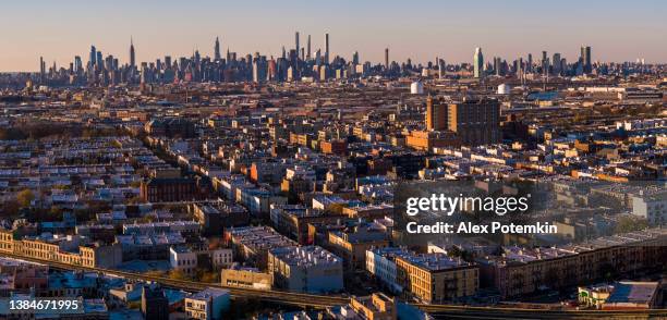 manhattan midtown skyline comprende l'empire state building, hudson yards e altri grattacieli iconici. vista sul quartiere residenziale di bushwick, brooklyn, al tramonto.   panorama cucito extra-large ad alta risoluzione. - bushwick foto e immagini stock