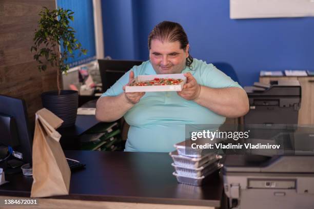 smiling overweight man looking closely at his pizza lunch - chef smelling food stockfoto's en -beelden