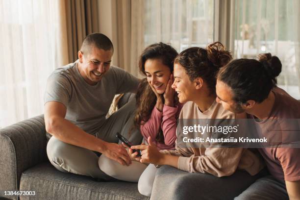 young friends sitting on sofa with smartphone and smiling. - friends laughing at iphone video stock pictures, royalty-free photos & images