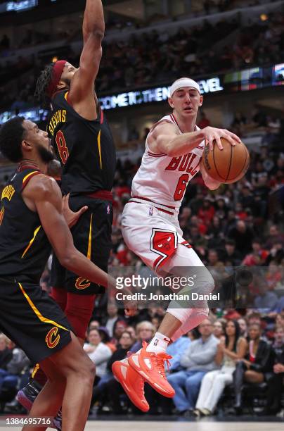 Alex Caruso of the Chicago Bulls leaps to pass around Lamar Stevens and Evan Mobley of the Cleveland Cavalier at the United Center on March 12, 2022...