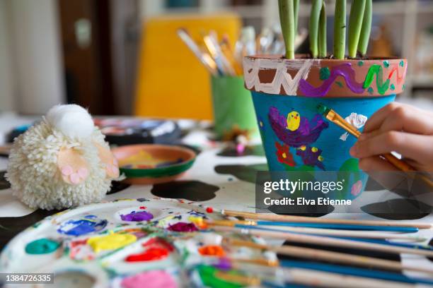 close-up of a child painting springtime themed terracotta plant pots on a dining table. - painting pottery stock pictures, royalty-free photos & images