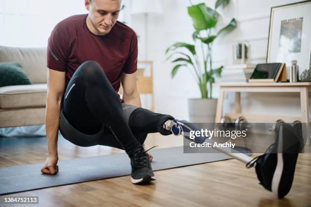 young man with prosthetic leg stretching before starting exercises at home - robotics alive stock pictures, royalty-free photos & images