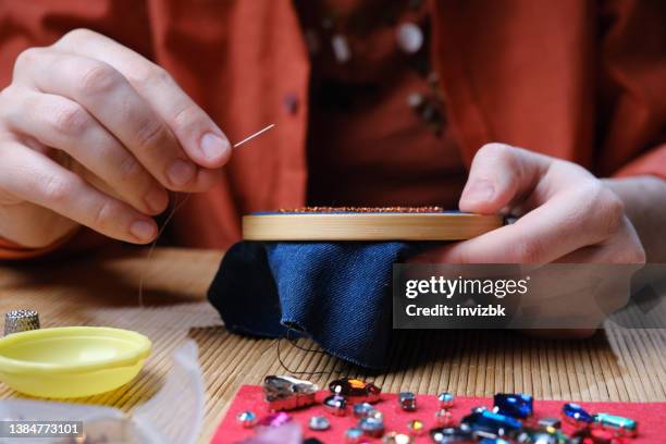 mains d’une femme mûre assise au bureau et fabriquant des bijoux en perles et en cristal à la maison - broderie photos et images de collection