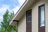 Single gable close-up with white soffit, fascia, beige vinyl siding on apartment building with several dormer windows with neutral sky background