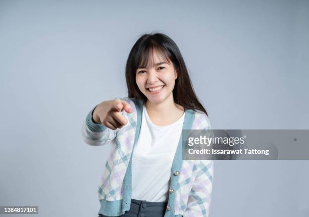 young woman points finger at you while smiling over isolated background - alternative view portraits stock-fotos und bilder