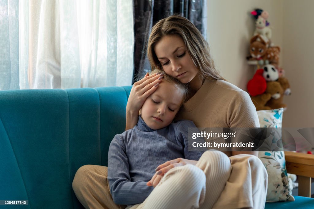 Woman and sad little daughter are sitting on couch and hugging