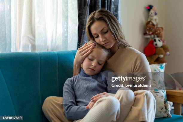 woman and sad little daughter are sitting on couch and hugging - sad mom stock pictures, royalty-free photos & images
