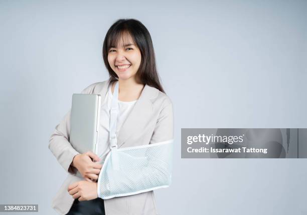 gorgeous young woman with an arm sling typing on the laptop after a having an accident and a broken bone - gypsum stock pictures, royalty-free photos & images