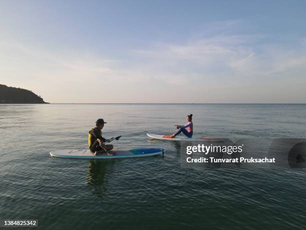 asian friends paddling on the water, enjoying their free time at the seaside. - paddle board stock pictures, royalty-free photos & images