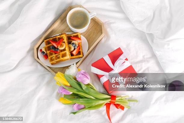 top view on holiday breakfast on bed. delicious branch - coffee, belgian waffles, gift box and fresh tulips - belgium waffles stock pictures, royalty-free photos & images