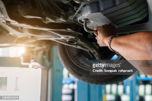 caucasian car mechanic under vehicle looking for potential issues with a drivetrain. automotive industry. - marcare foto e immagini stock