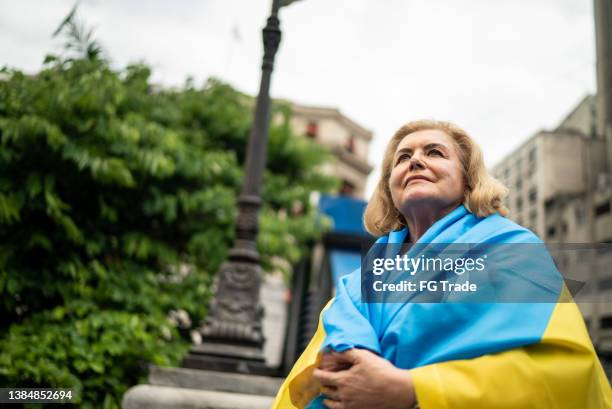 senior woman wearing ukranian flag and contemplating outdoors - ukrainian culture stock pictures, royalty-free photos & images