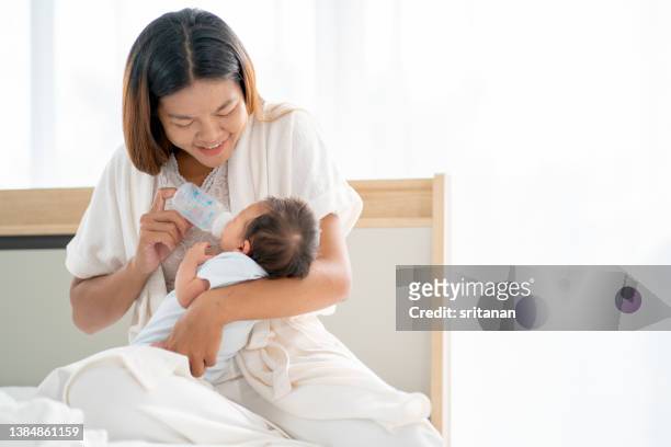 asian mother hold newborn baby on her chest and give bottle of milk to baby and they stay in bedroom with day light - chest kissing 個照片及圖片檔