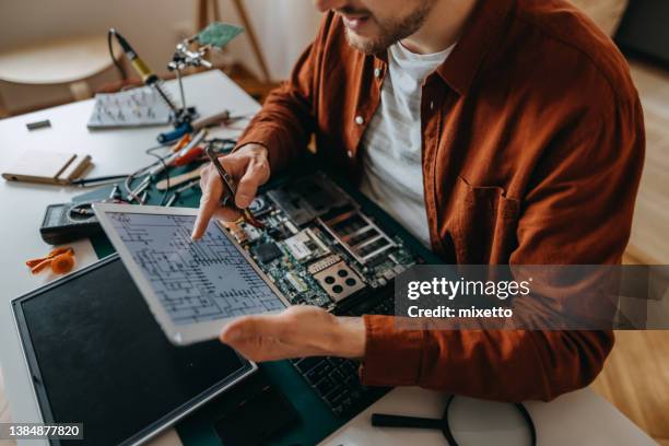 young man using digital tablet while examining laptop at home - magnifying glass laptop stock pictures, royalty-free photos & images