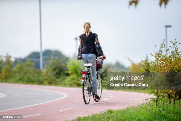 young woman riding her bicycle uphill on bicycle lane through public park - cykelbana bildbanksfoton och bilder