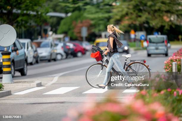 junge frau, die ihr fahrrad über die straße schiebt - zebrastreifen stock-fotos und bilder