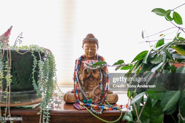 buddha sculpture draped in beads placed among house plants - representación humana fotografías e imágenes de stock