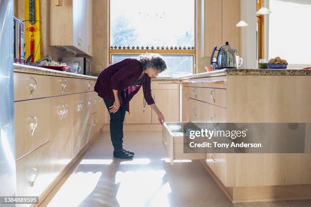 woman looking in kitchen drawer while preparing a meal - leaning over stock-fotos und bilder