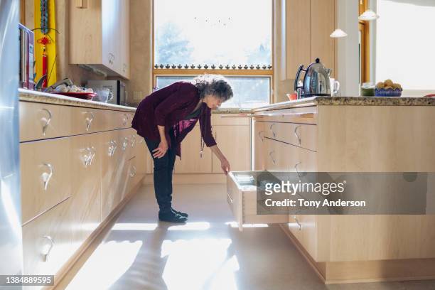 woman looking in kitchen drawer while preparing a meal - bukken stockfoto's en -beelden