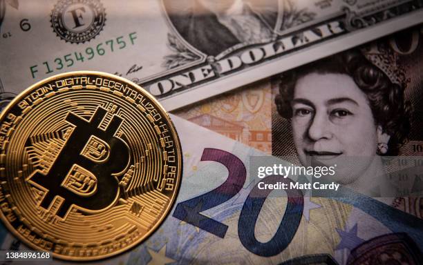 In this photo illustration a novelty Bitcoin token is photographed with a Sterling British Pound GBP, US dollar and a Euro bank note, on March 13,...