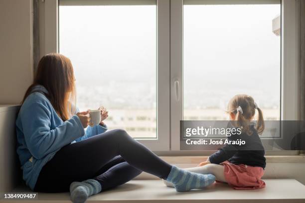 mother and daughter looking out of the bedroom window on a rainy day - criança stock pictures, royalty-free photos & images